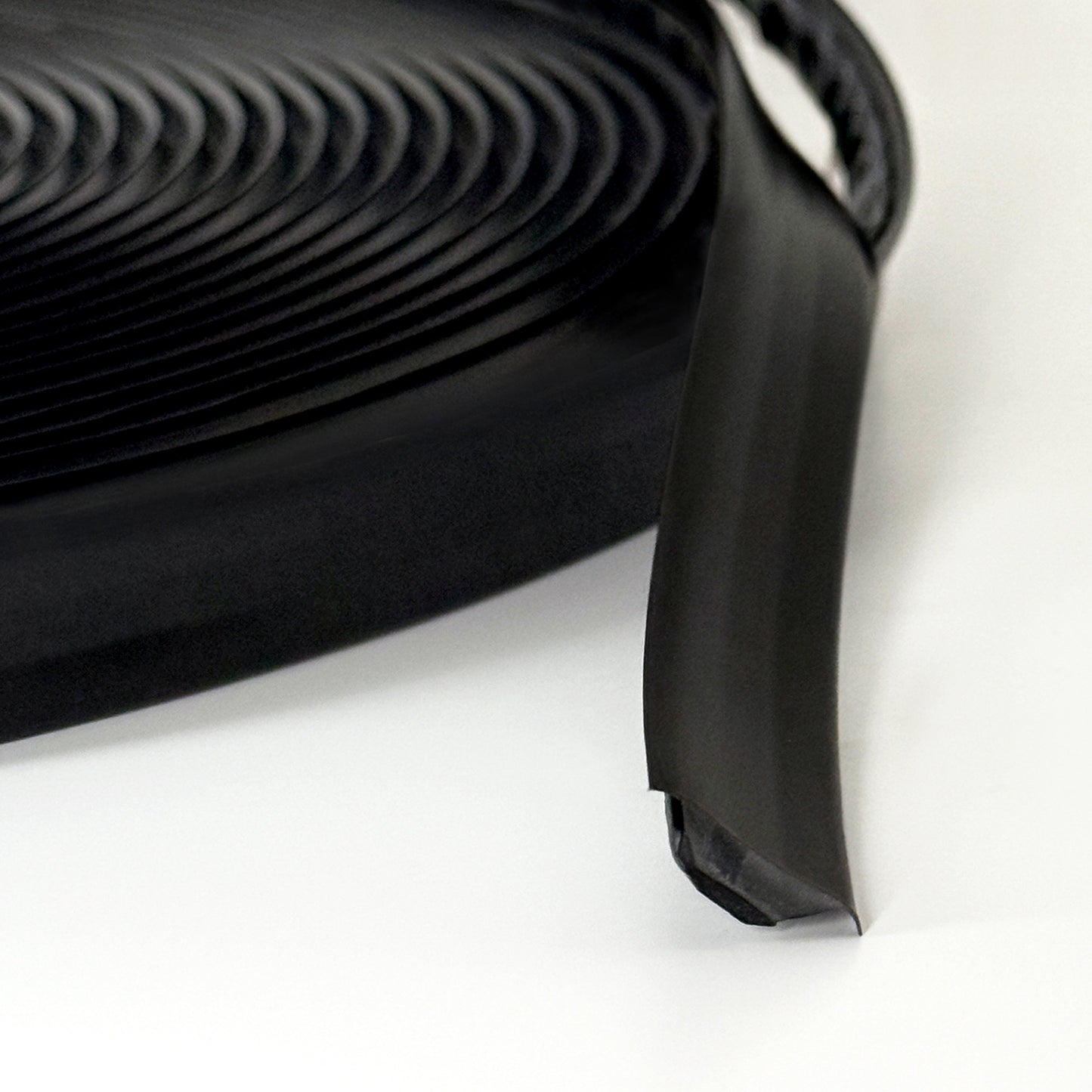 Close-up of black Smarter Trim roll with adhesive backing partially exposed.